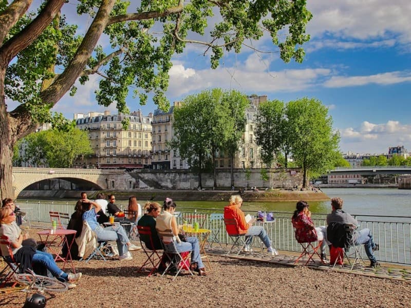 Ľudia sedia pri Seine v Paríži počas slnečného dňa.