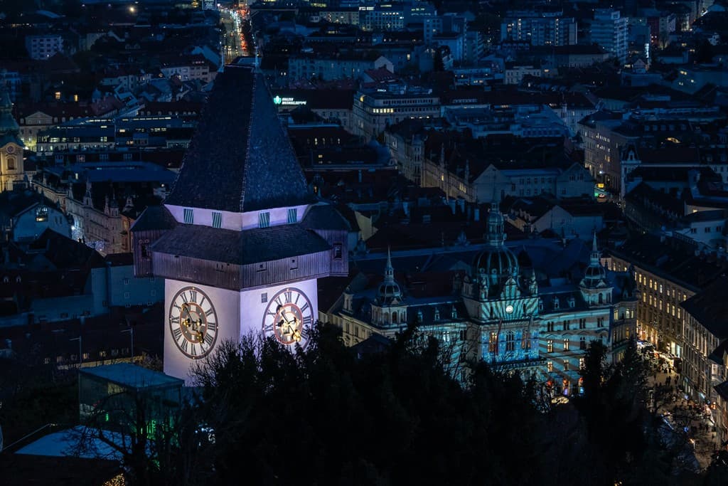 Veža hodinová a vysvietené mesto Graz.