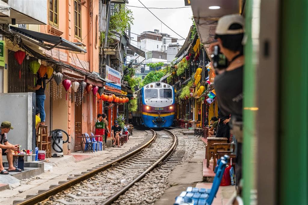 Vlak prechádza cez úzku uličku s kaviarničkami na Train Street v Hanoji